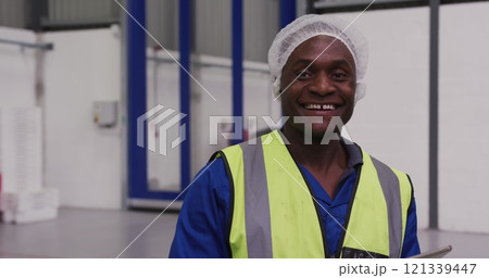 Portrait of a happy African American male worker working in a busy factory warehouse, wearing a hair Portrait of a happy African American male worker working in a busy factory warehouse, wearing a hair 121339447