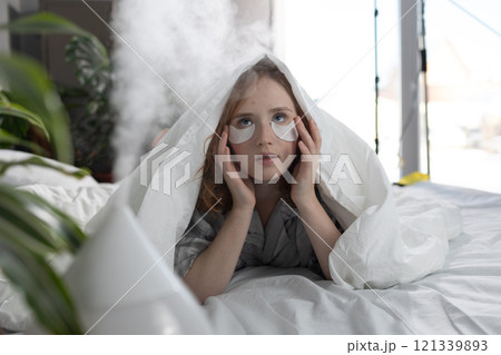 A woman is comfortably laying in her bed with soft eye patches over her face A woman is comfortably laying in her bed with soft eye patches over her face 121339893
