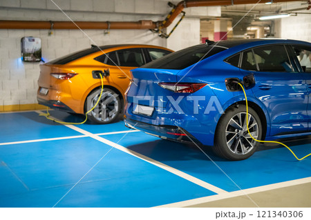 Two electric cars are charging in a well lit parking garage at the shopping mall Two electric cars are charging in a well lit parking garage at the shopping mall 121340306