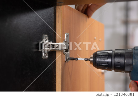 Worker fixing cabinet door hinge on cabinets. Worker fixing cabinet door hinge on cabinets. 121340391