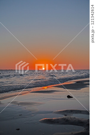Breathtaking ocean sunset with vivid orange sky, gentle waves, and serene beach shoreline 121342614