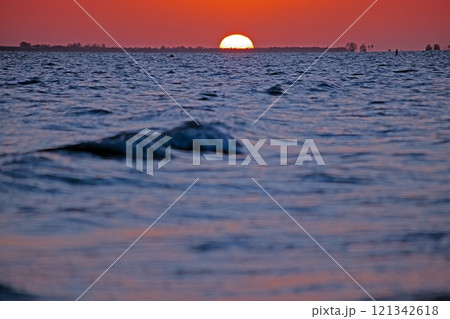 Breathtaking ocean sunset with vivid orange sky, gentle waves, and serene beach shoreline 121342618