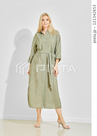 Beautiful woman posing in a green patterned maxi dress with high heels on a white background 121342653