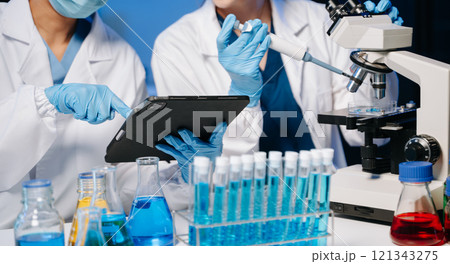 Young scientists conducting research investigations in a medical laboratory, a researcher in the foreground is using a microscope in laboratory Young scientists conducting research investigations in a medical laboratory, a researcher in the foreground is using a microscope in laboratory 121343275