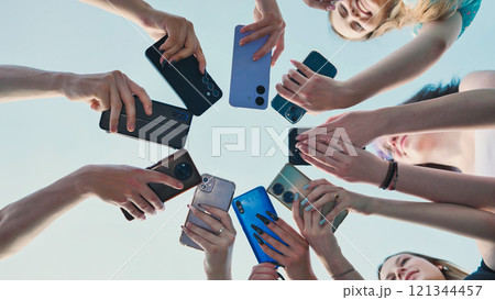Students gather in a circle outdoors during summer, using their smartphones to share and connect through technology 121344457