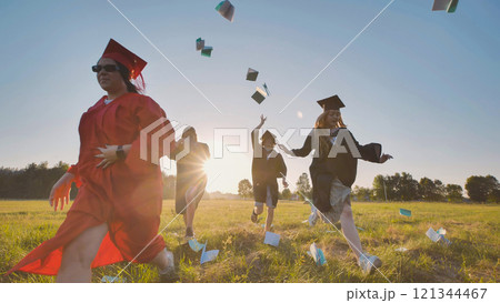 Group of joyful graduates celebrating their academic achievement by running in a field and tossing their graduation caps at sunset Group of joyful graduates celebrating their academic achievement by running in a field and tossing their graduation caps at sunset 121344467