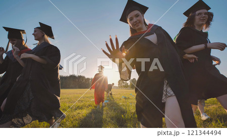 High school graduates joyfully running through a field at sunset, commemorating their academic success High school graduates joyfully running through a field at sunset, commemorating their academic success 121344494