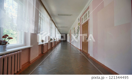 Walking down a long. Empty school corridor on the last day of school. Sunlight streams through windows. Casting a warm glow on wood floors and walls. Creating a calm 121344495