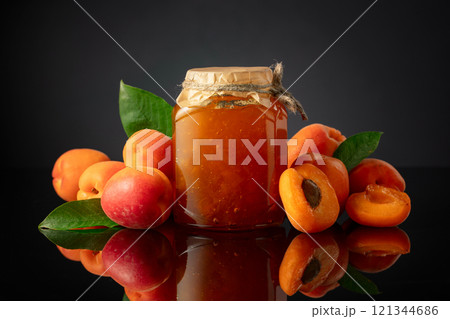 Apricot jam in glass jar and fresh fruits on a black reflective background. Apricot jam in glass jar and fresh fruits on a black reflective background. 121344686