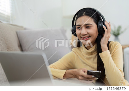 Young Girl Enjoying Music with Headphones While Relaxing at Home and Using a Laptop 121346279