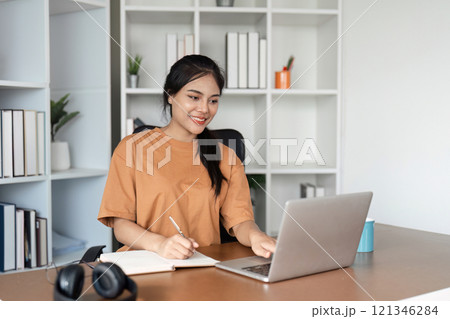Young Girl Studying Online from Home with Laptop and Notebook in Modern Home Office Setting 121346284