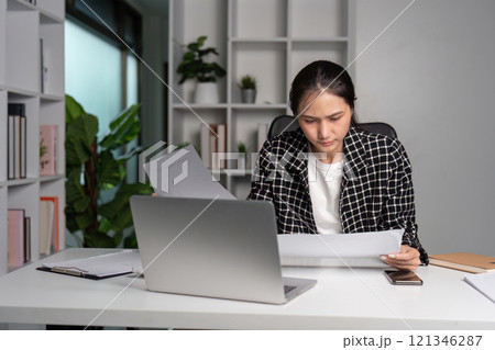 Young Accountant Experiencing Stress While Working at Desk with Laptop and Documents in Modern Office Setting 121346287