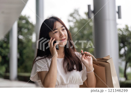Young Woman Shopping Outdoors with Paper Bag and Smartphone in Urban Setting on a Bright Day Young Woman Shopping Outdoors with Paper Bag and Smartphone in Urban Setting on a Bright Day 121346299