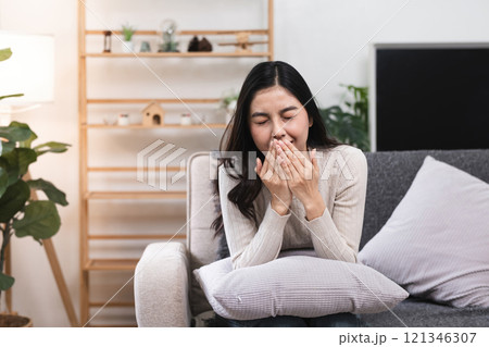 Young Woman Feeling Unwell on Sofa at Home, Sneezing and Covering Mouth, Battling Cold or Flu in Cozy Living Room Setting Young Woman Feeling Unwell on Sofa at Home, Sneezing and Covering Mouth, Battling Cold or Flu in Cozy Living Room Setting 121346307