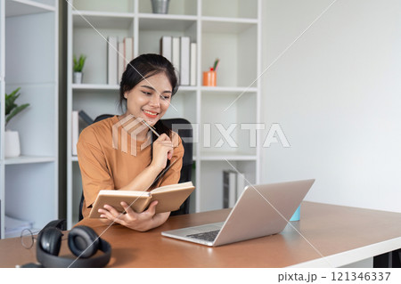 Young Woman Studying Online at Home with Laptop and Notebook, Engaged in E-Learning and Remote Education 121346337
