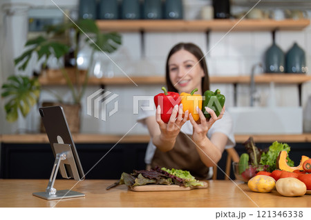 Young Woman Preparing a Healthy Salad with Fresh Vegetables in a Modern Kitchen, Smiling and Holding Bell Peppers 121346338
