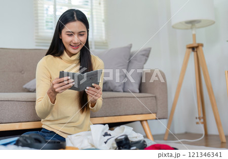 Young Woman Preparing Passport for Exciting Tourist Trip at Home, Smiling and Packing Essentials Young Woman Preparing Passport for Exciting Tourist Trip at Home, Smiling and Packing Essentials 121346341