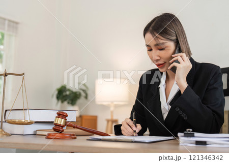 Young Female Lawyer Discussing Business Contract Law Over Phone While Reviewing Documents in Modern Office 121346342
