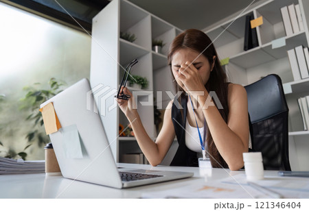 Stressed Businesswoman at Office Desk Experiencing Work Fatigue and Overwhelm in Modern Workplace Environment 121346404