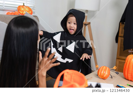 Mother and Daughter Decorating Living Room for Halloween with Pumpkins and Costumes, Creating Festive and Fun Atmosphere 121346430