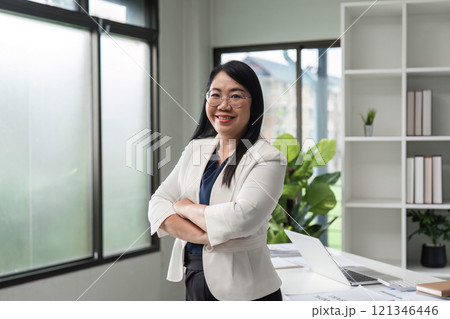 Confident Business Woman Standing in Modern Office with Arms Crossed, Smiling and Looking at Camera 121346446