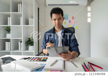 Young Male Graphic Designer Focused on Creative Work at Modern Office Desk with Computer and Design Tools Young Male Graphic Designer Focused on Creative Work at Modern Office Desk with Computer and Design Tools 121346499