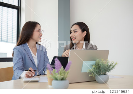 Two Female Accountant Collaborating on Financial Graphs and Data Analysis in a Modern Office Setting 121346624