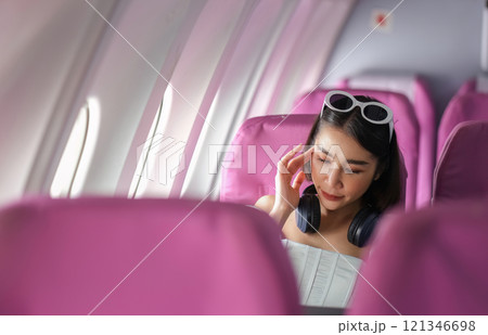 Woman Traveling by Plane, Relaxing in Comfortable Seat with Headphones, Enjoying In-Flight Entertainment, Modern Air Travel Experience 121346698