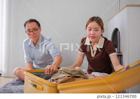 Father and Daughter Folding Clothes and Packing Suitcase Together in Modern Home for Family Travel Preparation 121346700