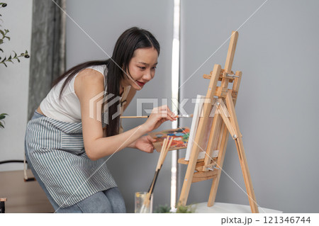 Young Woman Drawing Picture on Easel Relaxing in Modern Room with Natural Light and Comfortable Atmosphere 121346744
