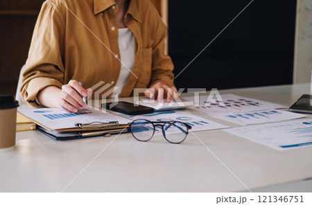 Young Businesswoman Analyzing Financial Documents at Modern Office Desk with Charts and Graphs 121346751