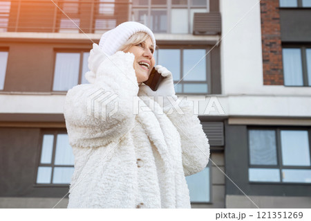 Smiling senior woman wearing winter clothes making a phone call outside a building 121351269