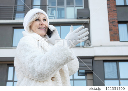 Elegant senior woman talking on phone in front of modern building in winter Elegant senior woman talking on phone in front of modern building in winter 121351300