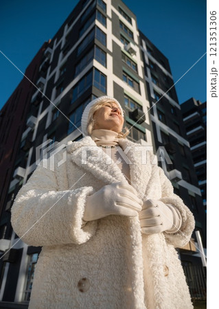 Smiling senior woman wearing winter clothes standing near modern building 121351306