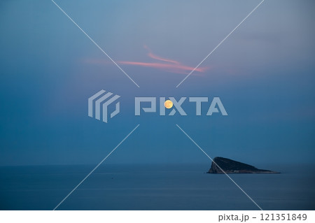 Serene full moon over calm ocean at dusk with small island in Benidorm, Spain. 121351849