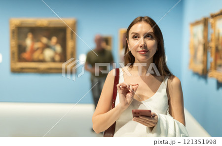 Woman with phone in the hall with paintings 121351998