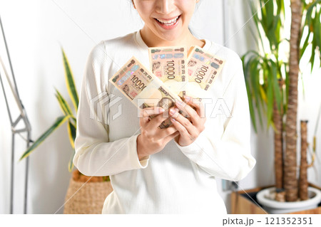 室内で札束を持つ笑顔の若いアジア人女性 121352351