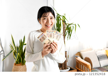 室内で札束を持つ笑顔の若いアジア人女性 121352418