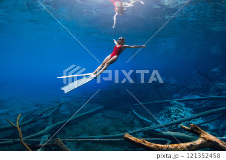 Freediver woman swims underwater with fins over sunken logs in the transparent lake. Free diving in blue crystal lake Freediver woman swims underwater with fins over sunken logs in the transparent lake. Free diving in blue crystal lake 121352458