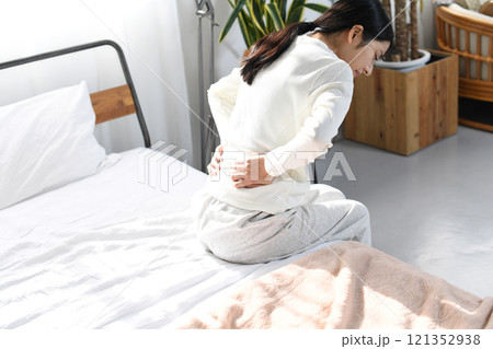 ベッドの上で腰痛や背痛に悩むアジア人女性 121352938