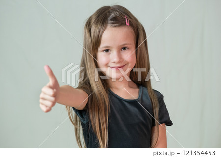 Close-up portrait of happy smiling little girl with long hair showing super sign with her thumbs up. Close-up portrait of happy smiling little girl with long hair showing super sign with her thumbs up. 121354453