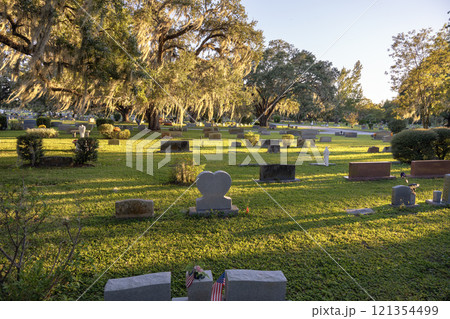 Cemetery graveyard with many tombstones at sunset. Burial place under southern oak trees on green grass in Orlando, Florida Cemetery graveyard with many tombstones at sunset. Burial place under southern oak trees on green grass in Orlando, Florida 121354499