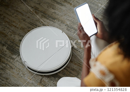 High angle shot of unrecognizable woman with smartphone setting robot vacuum cleaner 121354828