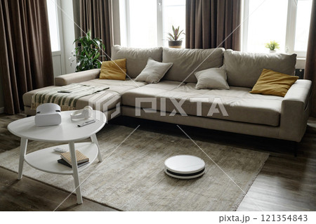 High angle shot of white robot vacuum cleaning beige rug in living room with comfortable couch High angle shot of white robot vacuum cleaning beige rug in living room with comfortable couch 121354843