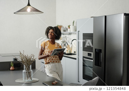 African American woman with tablet in hands looking at kitchen lamp while setting bulb brightness 121354848