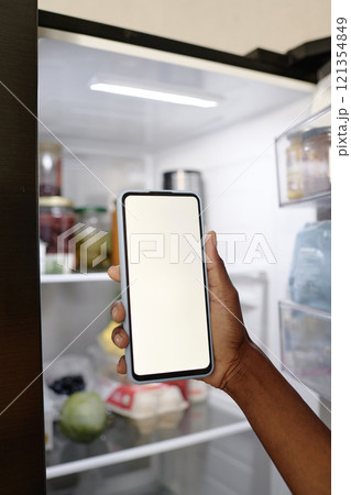 Unrecognizable female hand holding smartphone with launched app for smart fridge Unrecognizable female hand holding smartphone with launched app for smart fridge 121354849
