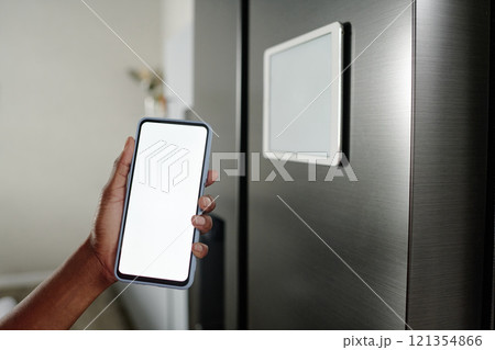 Unrecognizable female hand demonstrating smartphone with white screen near refrigerator Unrecognizable female hand demonstrating smartphone with white screen near refrigerator 121354866