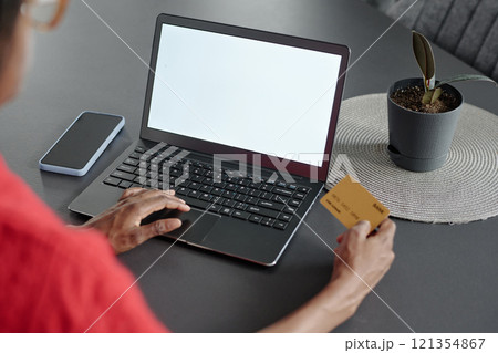 High angle shot of graphite table with laptop, smartphone and plant in clay pot on top, unrecognizable woman holding golden credit card 121354867