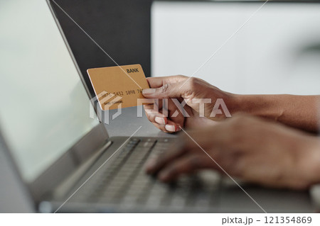 Medium close up of golden credit card in unrecognizable female hand, blurred laptop in foreground Medium close up of golden credit card in unrecognizable female hand, blurred laptop in foreground 121354869