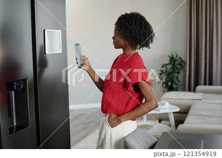 Side view shot of African American skinny woman using smartphone to connect with app for smart kitchen appliances 121354919